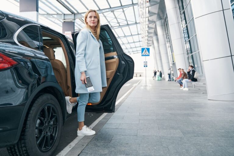 Businesswoman exiting a luxury car at the airport, representing Top Class Chauffeurs' premium airport transfer service