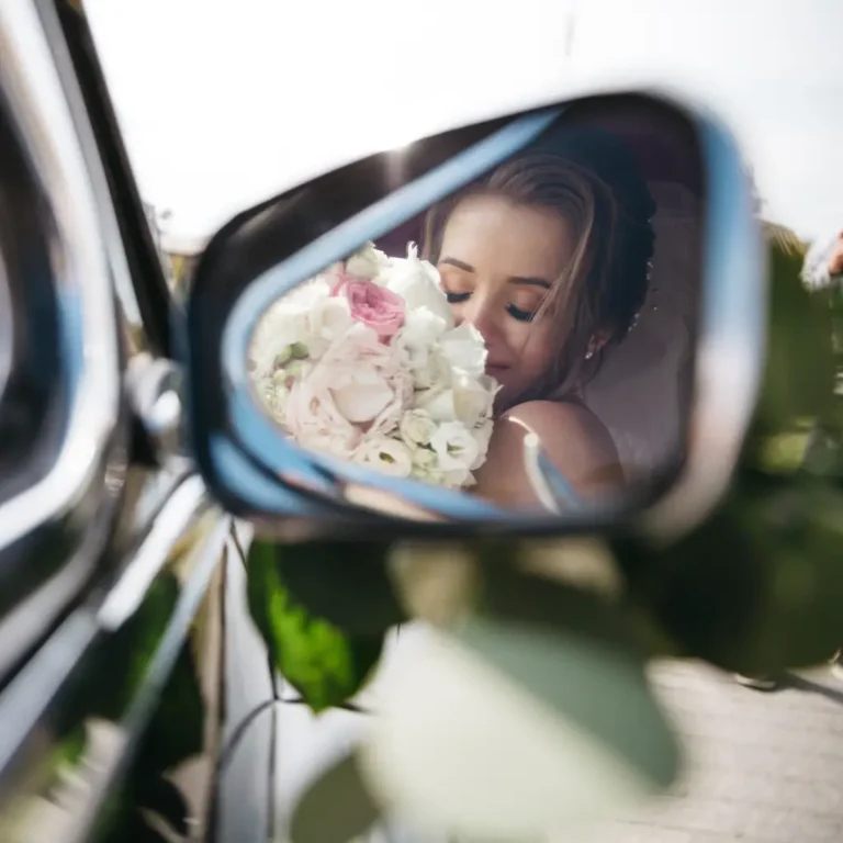 Bride reflected in a car mirror holding a soft pastel bouquet, symbolizing elegance and luxury wedding limo car service.
