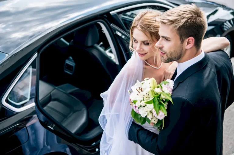 Bride and groom standing beside a luxury wedding limo car, preparing for their elegant wedding transportation service.